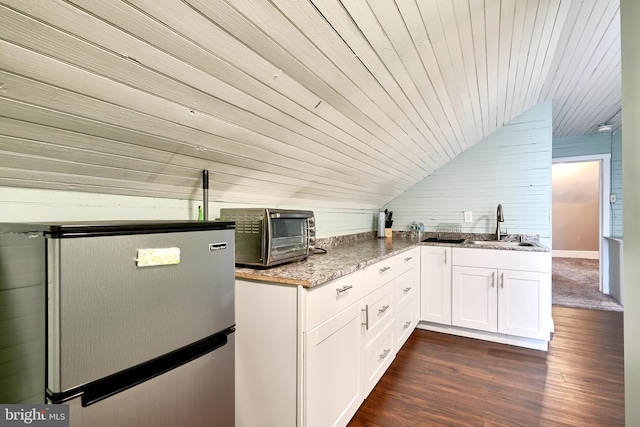 kitchen with wood walls, wooden ceiling, white cabinets, sink, and stainless steel fridge