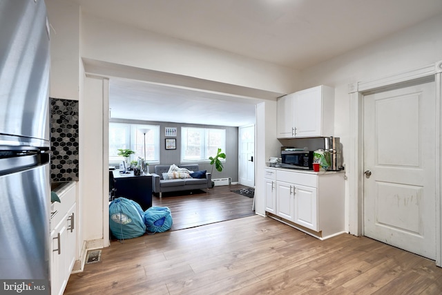 kitchen featuring appliances with stainless steel finishes, light wood-type flooring, a baseboard radiator, and white cabinetry