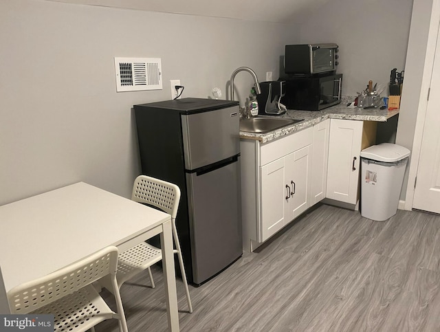 kitchen featuring stainless steel fridge, light hardwood / wood-style floors, white cabinetry, and sink