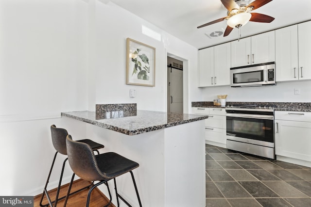 kitchen with appliances with stainless steel finishes, a barn door, a kitchen breakfast bar, and white cabinetry