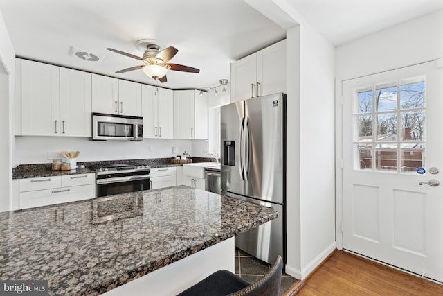 kitchen featuring dark stone counters, stainless steel appliances, white cabinetry, and a breakfast bar