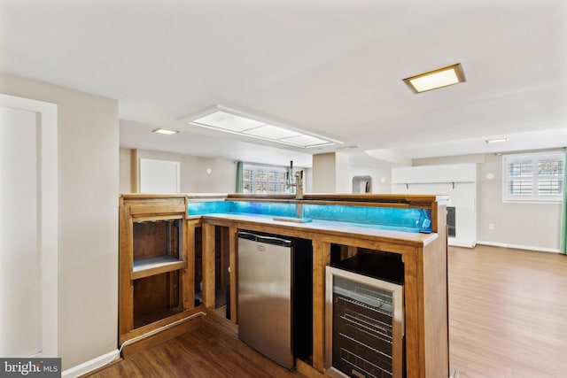 bar featuring stainless steel refrigerator, a healthy amount of sunlight, beverage cooler, and wood-type flooring