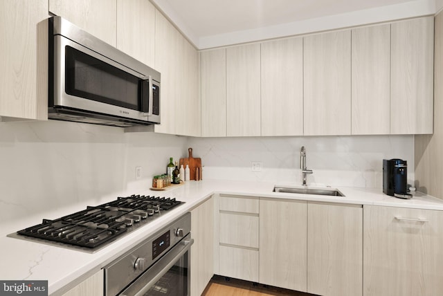 kitchen with light stone countertops, sink, stainless steel appliances, backsplash, and light brown cabinets