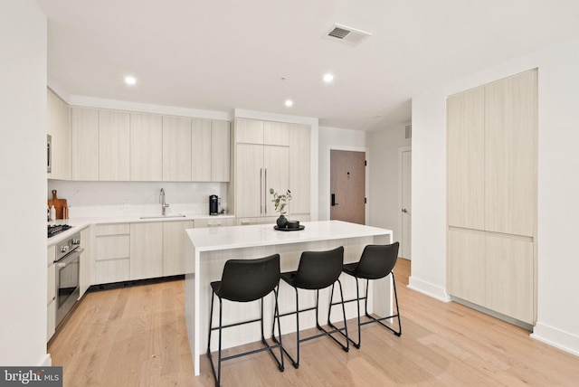 kitchen with sink, oven, a kitchen bar, light hardwood / wood-style flooring, and a kitchen island