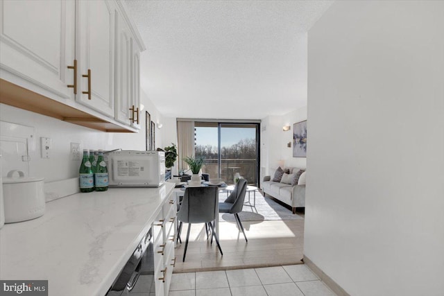 kitchen with light stone countertops, a textured ceiling, white cabinets, light tile patterned flooring, and expansive windows