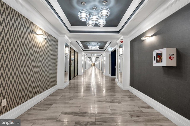 hall with a tray ceiling, ornamental molding, and an inviting chandelier