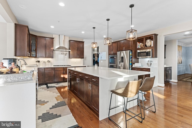 kitchen featuring wall chimney exhaust hood, sink, a center island, appliances with stainless steel finishes, and pendant lighting