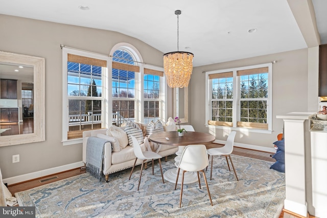 dining space with vaulted ceiling, hardwood / wood-style floors, and a notable chandelier