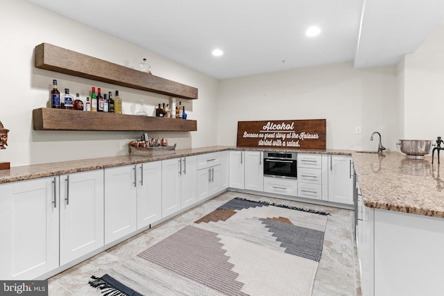 kitchen with light stone countertops, oven, sink, and white cabinets