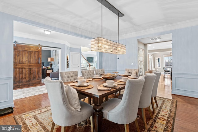 dining room featuring crown molding, an inviting chandelier, a barn door, and light hardwood / wood-style floors