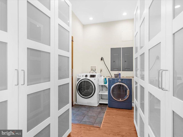 clothes washing area featuring washing machine and dryer, hardwood / wood-style flooring, and electric panel