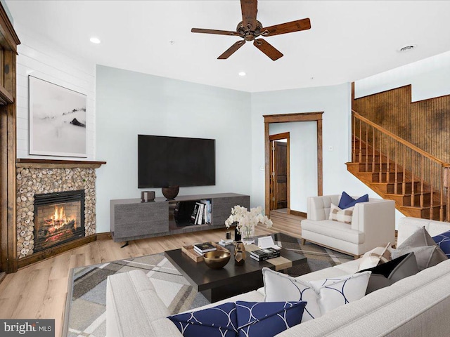 living room with light hardwood / wood-style flooring, ceiling fan, and a tiled fireplace