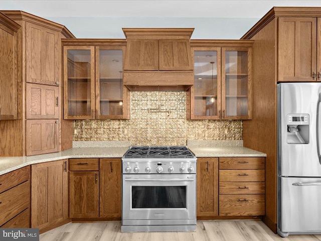 kitchen with light stone countertops, backsplash, light hardwood / wood-style floors, appliances with stainless steel finishes, and custom exhaust hood