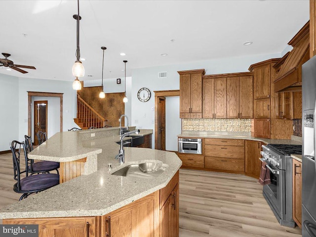 kitchen featuring a breakfast bar, sink, decorative light fixtures, stainless steel stove, and a large island