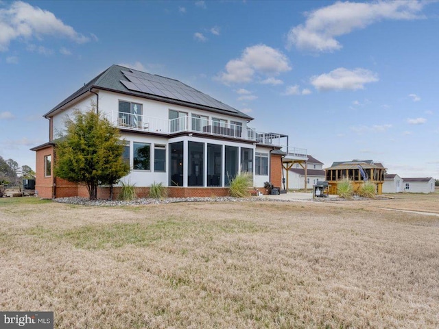 back of property with a lawn, a sunroom, and a balcony