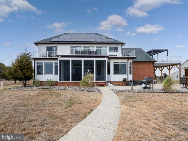 rear view of house featuring a lawn, a sunroom, a balcony, and a patio