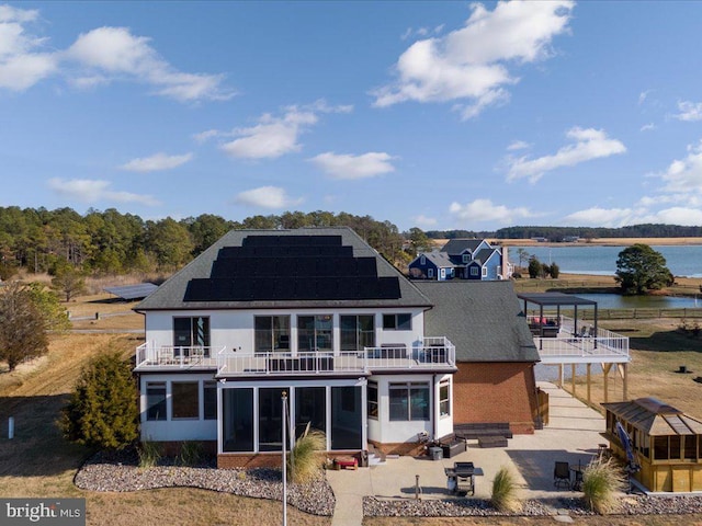 rear view of house with a sunroom, solar panels, a balcony, a patio area, and a water view