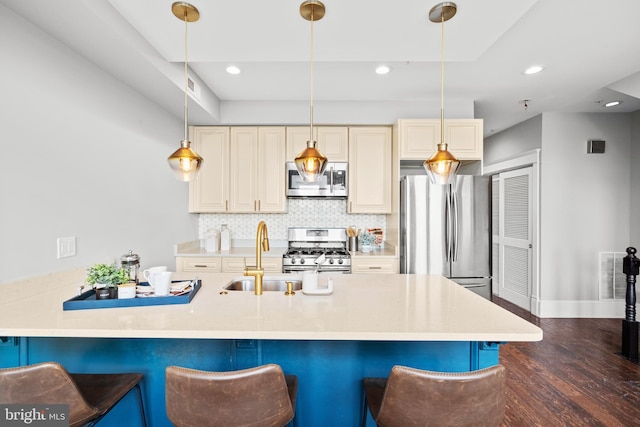 kitchen with decorative backsplash, stainless steel appliances, cream cabinets, hanging light fixtures, and a breakfast bar area