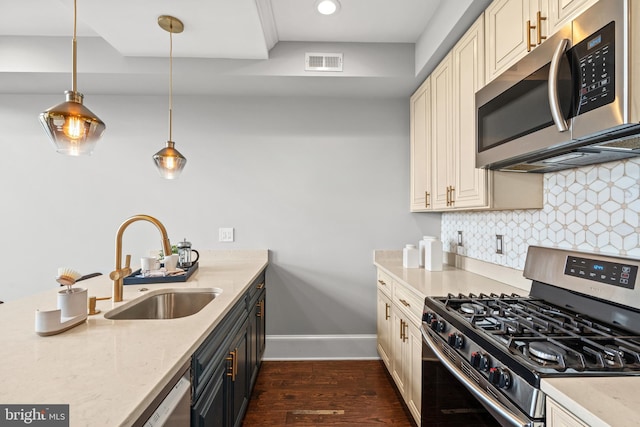 kitchen with appliances with stainless steel finishes, light stone counters, sink, cream cabinets, and pendant lighting