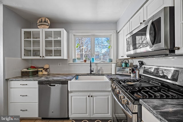 kitchen featuring sink, appliances with stainless steel finishes, white cabinets, decorative backsplash, and dark stone counters