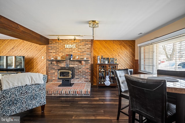 dining room with dark wood-type flooring, wooden walls, a wood stove, and rail lighting