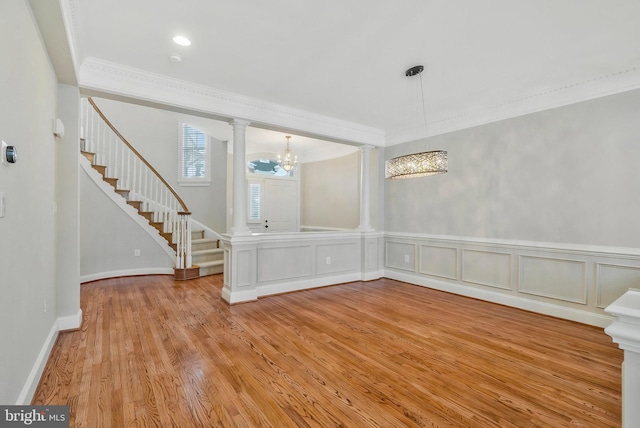 interior space featuring a notable chandelier, ornamental molding, decorative columns, and light wood-type flooring