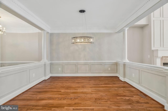 unfurnished dining area with crown molding, decorative columns, light hardwood / wood-style flooring, and a notable chandelier