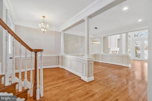 entrance foyer with a notable chandelier, crown molding, decorative columns, and light hardwood / wood-style floors