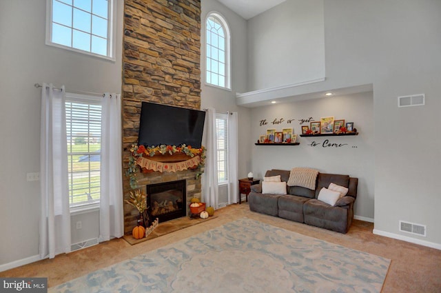 living room with a high ceiling, light colored carpet, and a stone fireplace