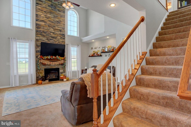 stairs with carpet flooring, ceiling fan, a towering ceiling, and a fireplace