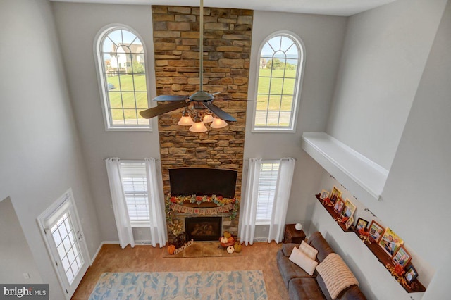 living room featuring a stone fireplace, ceiling fan, a towering ceiling, and a healthy amount of sunlight