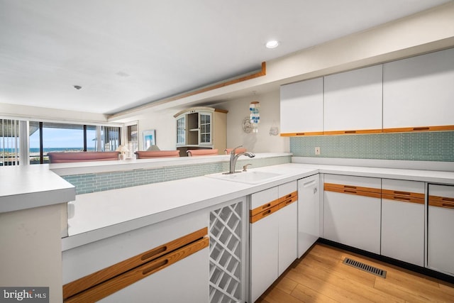 kitchen with white cabinets, sink, decorative backsplash, light wood-type flooring, and kitchen peninsula