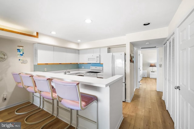 kitchen featuring white appliances, backsplash, kitchen peninsula, a kitchen bar, and white cabinetry