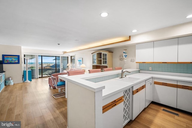 kitchen with white cabinets, kitchen peninsula, sink, and light hardwood / wood-style flooring