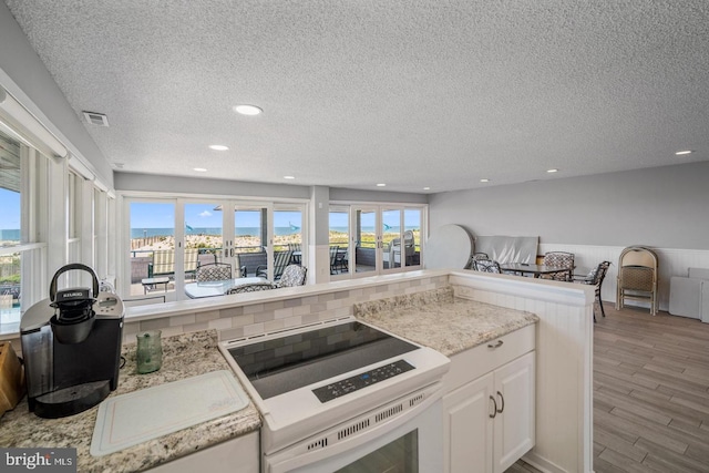 kitchen featuring kitchen peninsula, a textured ceiling, white cabinets, range, and light hardwood / wood-style floors