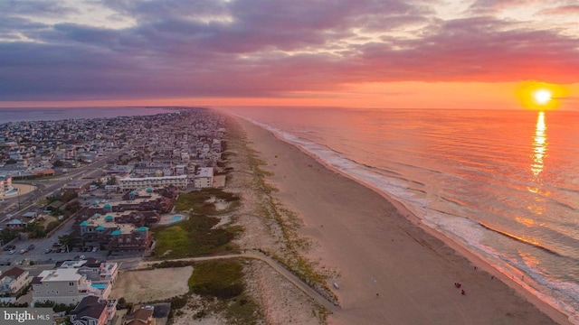 aerial view at dusk featuring a water view and a view of the beach