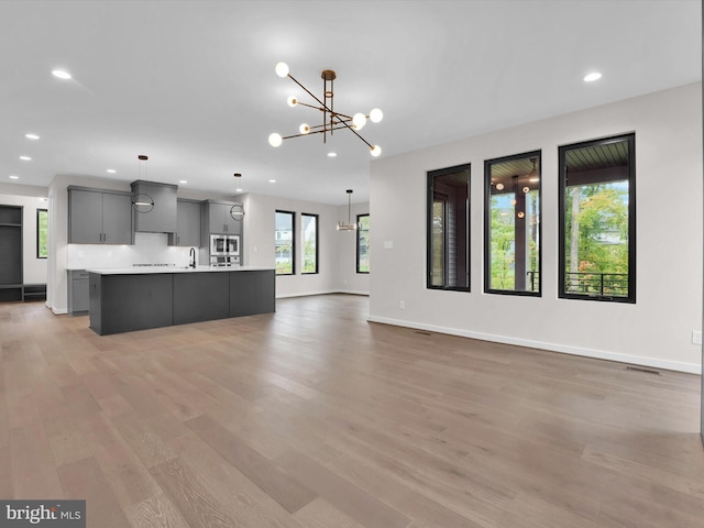 kitchen featuring a center island with sink, pendant lighting, gray cabinetry, and light hardwood / wood-style flooring