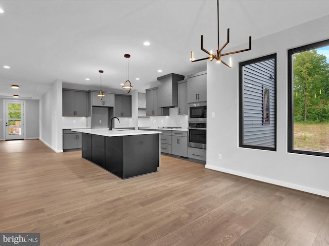 kitchen featuring gray cabinetry, pendant lighting, a center island with sink, tasteful backsplash, and a chandelier