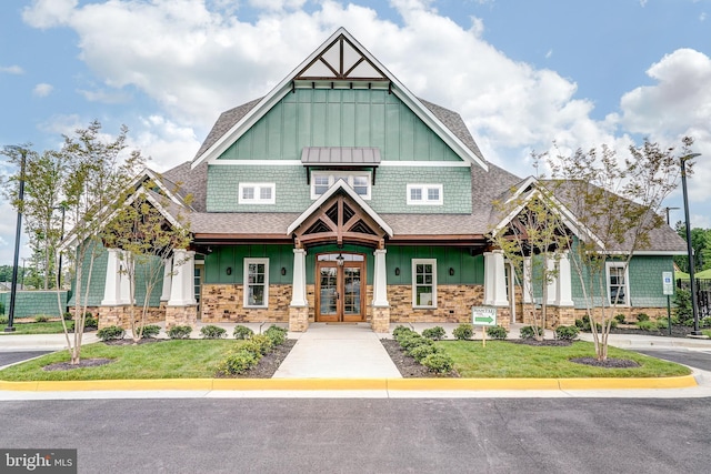 view of front of house with a front lawn, stone siding, board and batten siding, french doors, and roof with shingles