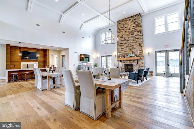 dining area featuring light wood-style floors, a stone fireplace, a high ceiling, and a healthy amount of sunlight