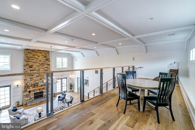 dining area featuring a stone fireplace, coffered ceiling, wood finished floors, and plenty of natural light