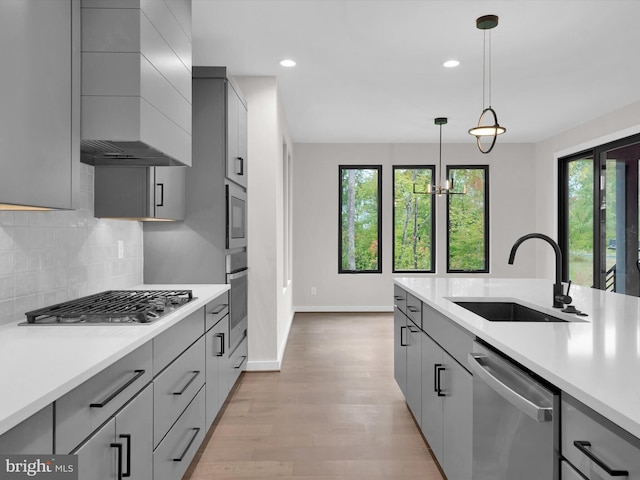 kitchen featuring sink, wall chimney exhaust hood, decorative light fixtures, gray cabinets, and appliances with stainless steel finishes