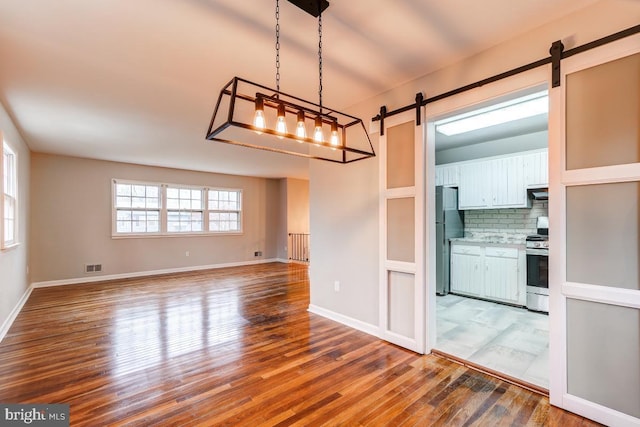 kitchen with hanging light fixtures, stainless steel appliances, tasteful backsplash, white cabinetry, and wood-type flooring