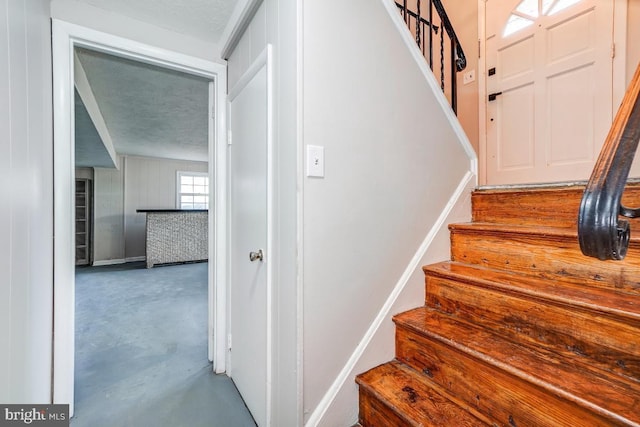 stairs with a textured ceiling and concrete flooring