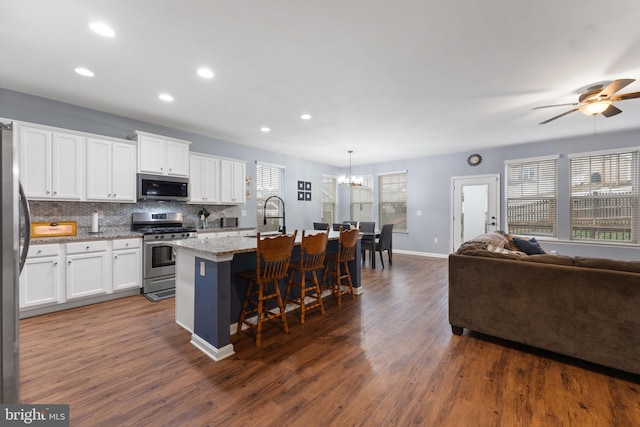 kitchen featuring white cabinets, appliances with stainless steel finishes, hanging light fixtures, a kitchen island with sink, and a breakfast bar area