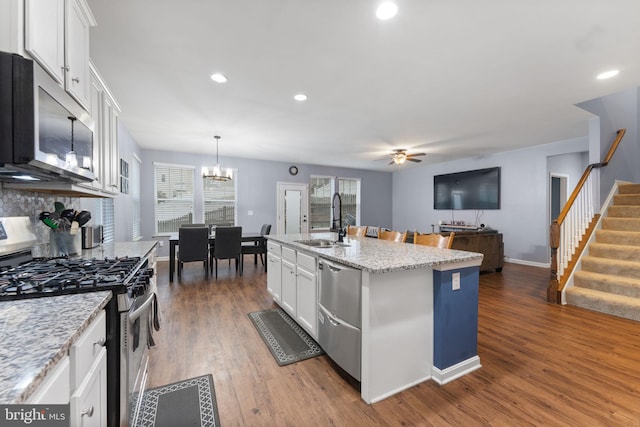 kitchen with pendant lighting, white cabinets, appliances with stainless steel finishes, an island with sink, and sink