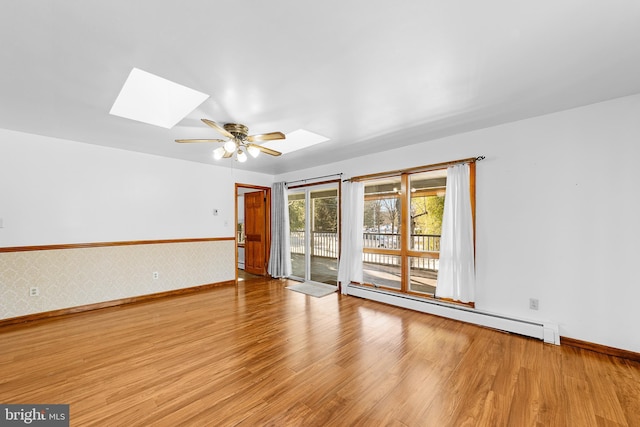 spare room with a skylight, light hardwood / wood-style flooring, ceiling fan, and a baseboard heating unit