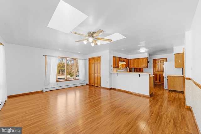 unfurnished living room featuring a skylight, ceiling fan, light hardwood / wood-style floors, and a baseboard heating unit