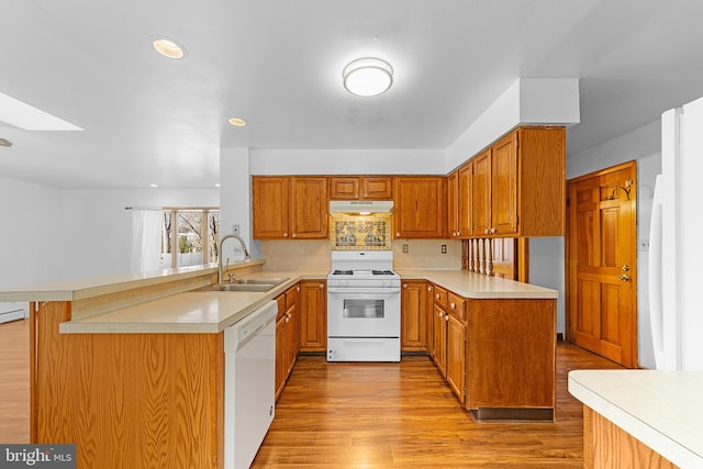 kitchen with kitchen peninsula, a skylight, white appliances, sink, and a breakfast bar area