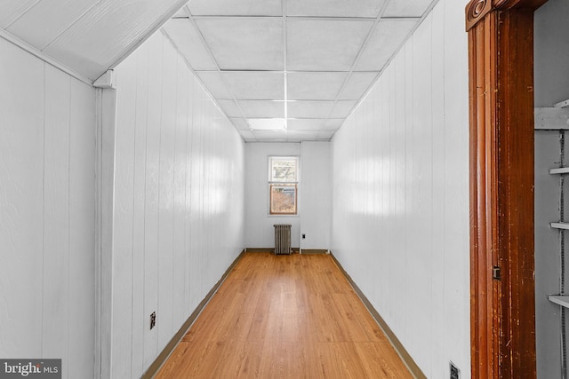 interior space with a drop ceiling, wood walls, light wood-type flooring, and radiator heating unit